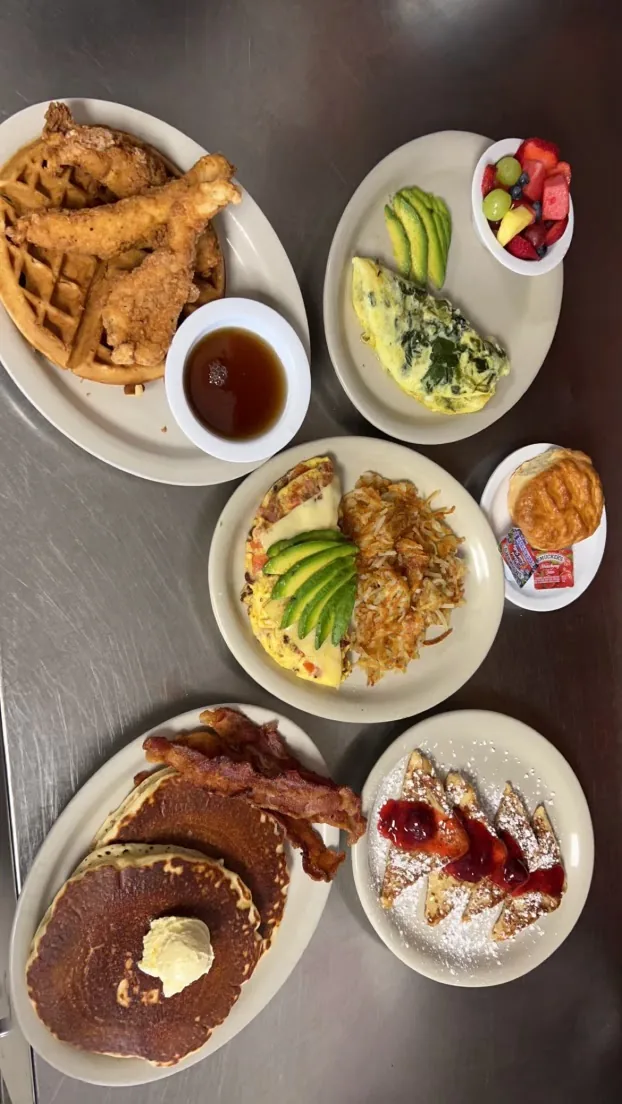 A spread of City Cafe breakfast plates including a waffle with fried chicken, omelets, hash browns and pancakes